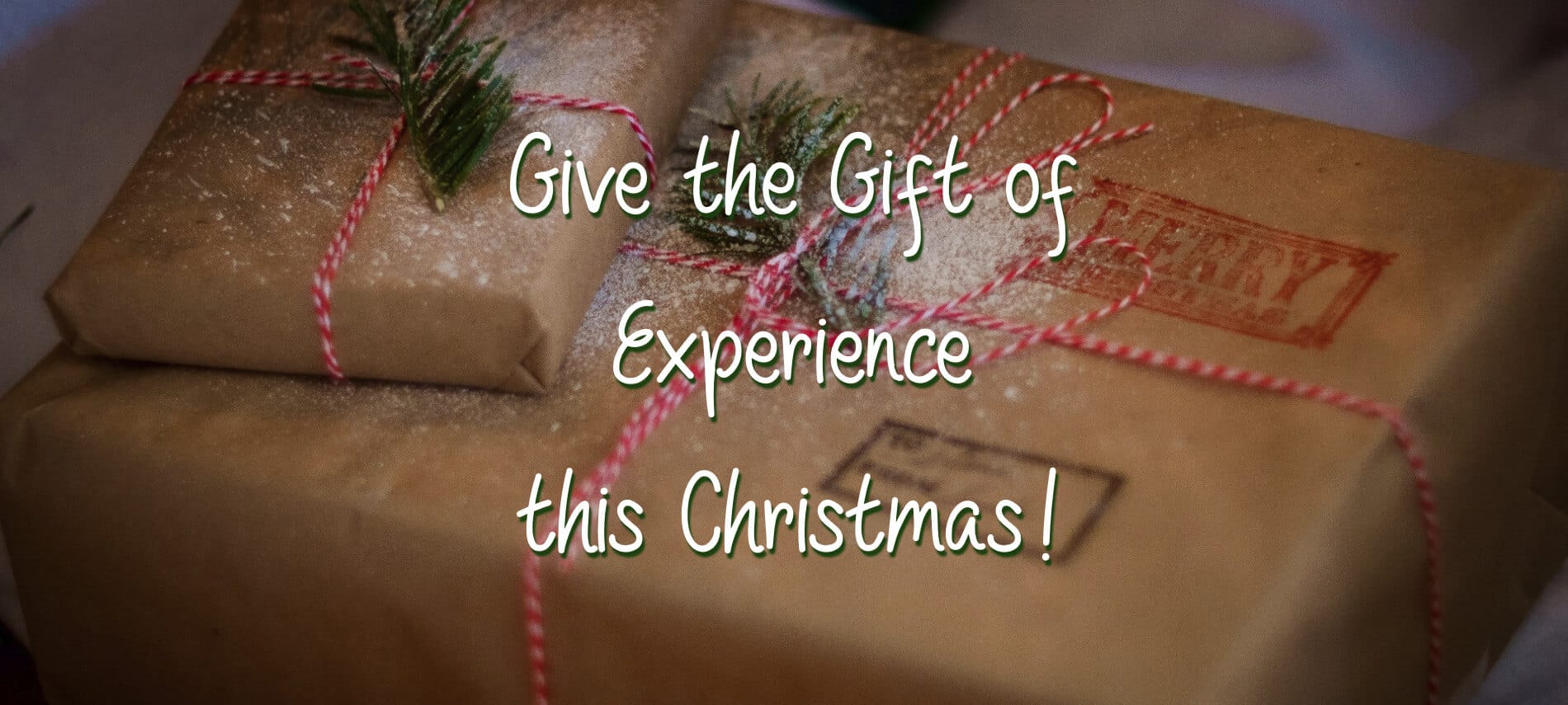 Two gifts wrapped in brown kraft paper and striped red and white string with the words, "Give the Gift of Experience this Christmas!"