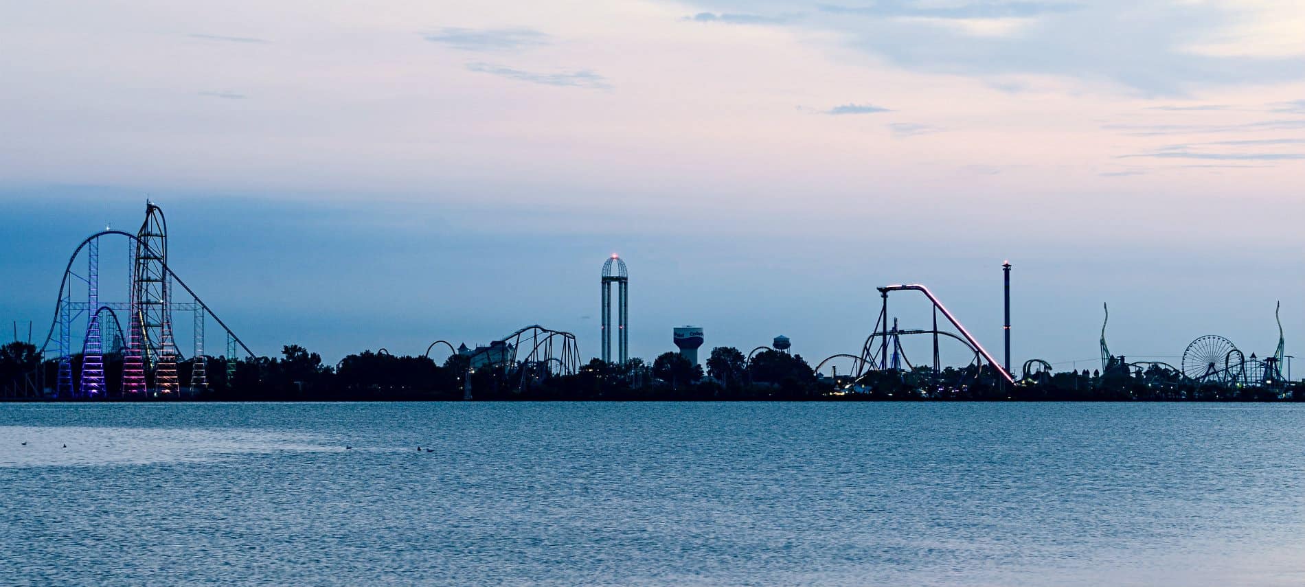 Large body of water with amusement park rides in the background lit up in colored lights