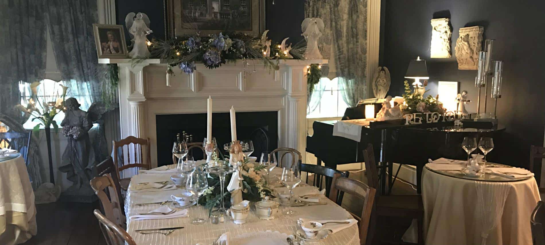 Elegant dining room with soft blueish gray walls and curtains, fireplace, baby grand piano, and tables set for a meal