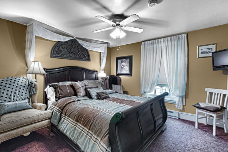 Serene guest room with tan walls, burgundy carpet, wooden sleigh bed, large window and side chairs