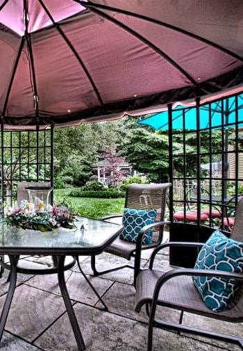 Rear patio with umbrella tables and chairs surrounded by lush green grass, plants and trees